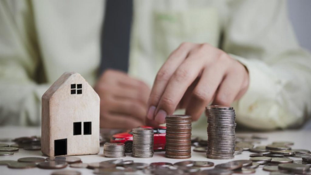 Rachat de crédits profession libérale : pièces de monnaie empilées à côté d'une maison et d'une voiture miniatures.
